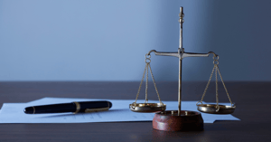 A close-up of tax forms and a pen, with a scale of justice in front of them on table