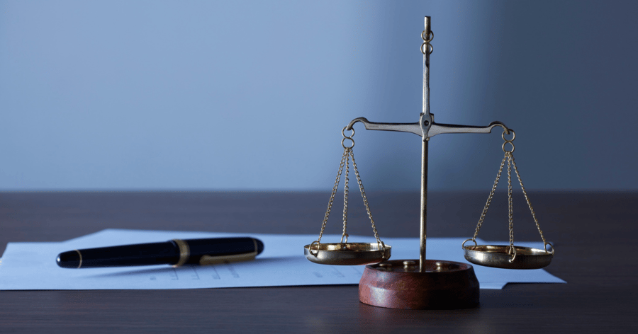 A close-up of tax forms and a pen, with a scale of justice in front of them on table